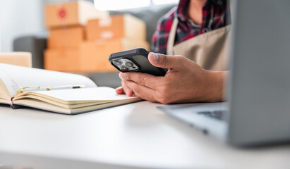 Fototapeta premium Entrepreneurs Small Business SME Independent men work at home Use smartphones and laptops for commercial checking, online marketing, packing boxes, SME sellers, concept, e-commerce team, online sales