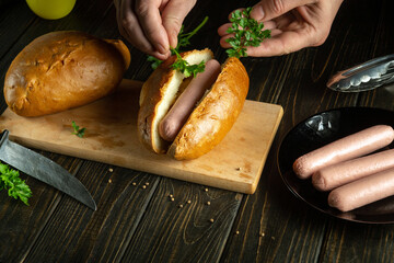 A street chef prepares a hot dog on the kitchen table. The concept of cooking fast food with buns and sausages