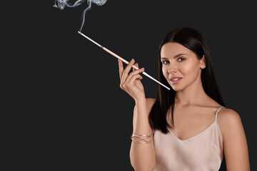 Obraz premium Woman using long cigarette holder for smoking on black background, space for text