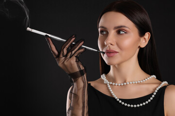 Fototapeta premium Woman using long cigarette holder for smoking on black background