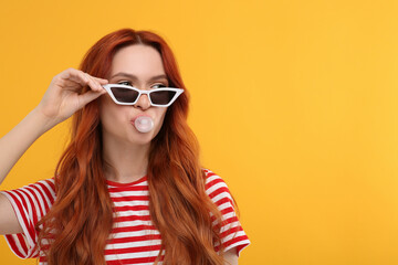 Beautiful woman in sunglasses blowing bubble gum on orange background. Space for text