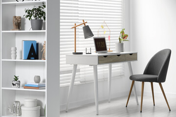 Cozy workspace with laptop, desk and comfortable chair at home. Stylish interior design