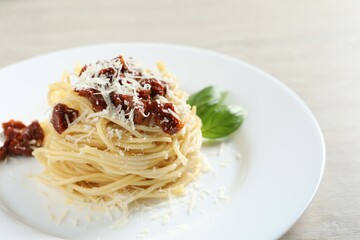 Tasty spaghetti with sun-dried tomatoes and parmesan cheese on wooden table, closeup. Exquisite presentation of pasta dish