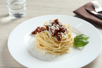 Tasty spaghetti with sun-dried tomatoes and parmesan cheese served on wooden table, closeup. Exquisite presentation of pasta dish