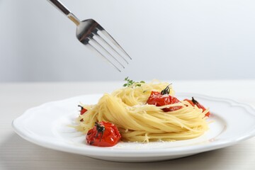 Eating tasty capellini with tomatoes and cheese at white wooden table, closeup. Exquisite presentation of pasta dish