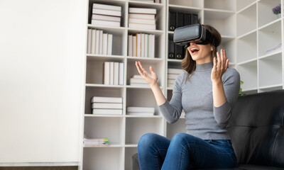 Surprised young latin woman in VR headset touching the air. Smiling caucasian woman wearing vr glasses virtual reality technology device watching 3d simulation video while sitting on sofa.