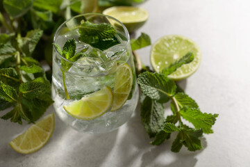Mojito with ice, lime, and mint on a white stone table.