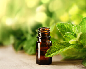 Essential oil in a brown glass jar with fresh mint leaves on wooden table