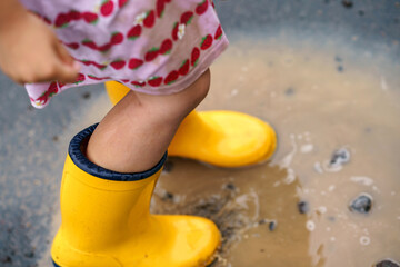 Close-up of little preschool girl wearing yellow rain boots and walking during puddles. Cute child...