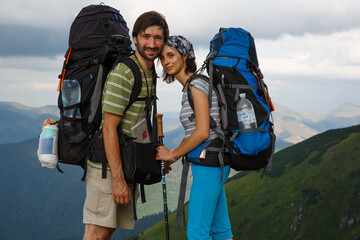 An affectionate couple with hiking backpacks stands forehead to forehead, deeply in love, set...