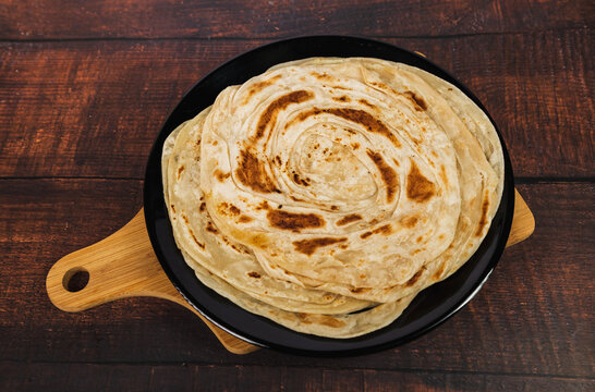 Kerala Parathas or Porotta Roti on a wooden table. Barotta naan is a layered flatbread made from maida whole wheat flour and it can be served with beef or chicken or egg or veg curry. Indian food.