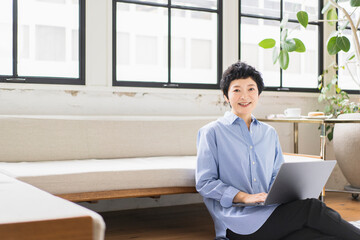 リラックスしながらパソコン作業をしている笑顔の日本人女性/カメラ目線