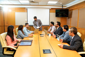 Indian ceo presenting project information to other businesspeople, using laptop and white board.