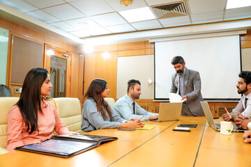 Indian ceo presenting project information to other businesspeople, using laptop and white board.