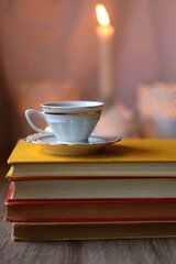 Cup of tea or coffee, plate of cookies, books, e-reader, pencil and lit candles on the table. Selective focus.