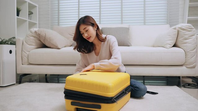 Young asian woman packing clothes and close the zipper yellow luggage bring mobile phone check in flight before the trip of long weekend holiday. Traveling and long weekend concept