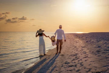 Fototapeten A happy family in walks hand in hand down a paradise beach during sunset tme and enjoys their summer vacation time © moofushi