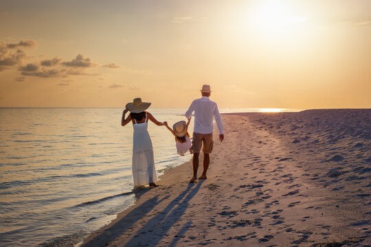A happy family in walks hand in hand down a paradise beach during sunset tme and enjoys their summer vacation time