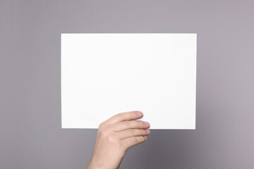 Obraz premium Woman holding sheet of paper on grey background, closeup. Mockup for design