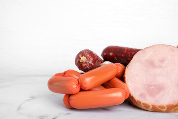 Different types of sausages on white marble table, space for text