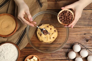 Cooking sweet cookies. Woman adding chocolate chips to dough at wooden table, top view