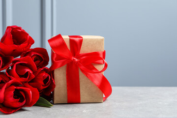 Beautiful gift box with bow and red tulip flowers on light table, space for text