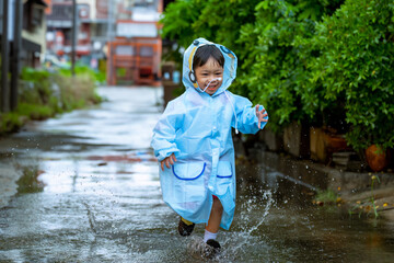 Asian boy wearing a raincoat outside the house. He is playing in the rain...