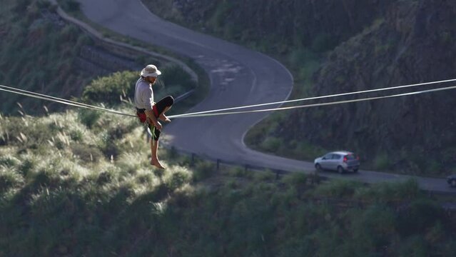 A man balancing on a highline contemplating a road with cars below. Slow motion.