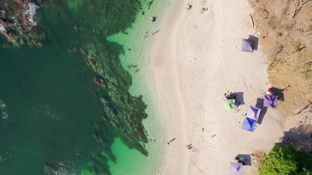 Top down drone lowering shots of umbrellas at the beach next to the clear ocean