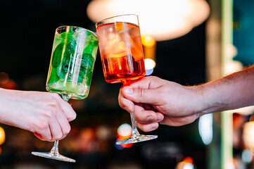 hands of man and women holding and clinking glasses cocktails in restaurant