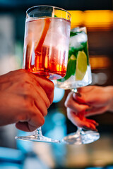 hands of man and women holding and clinking glasses cocktails in restaurant