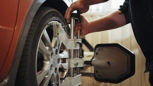 A car service employee installs a wheel adapter with a target on the wheel to perform a wheel alignment. Diagnostics and balancing of wheels of a lifting trolley at a modern service station