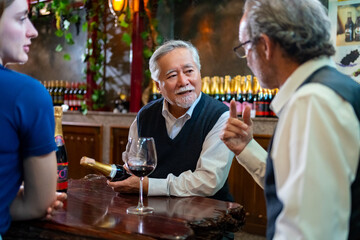 Professional senior man sommelier explaining and recommending wine to customer at wine shop or liquor store. Sommelier tasting wine in winery. Winery manufacturing industry and winemaker concept.