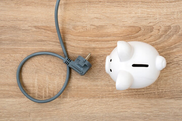 Piggy bank with a power plug on the wooden table