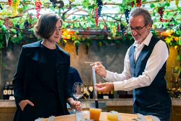 Professional senior man sommelier explaining and recommending wine to customer at wine shop or liquor store. Sommelier testing wine in winery. Winery manufacturing industry and winemaker concept.