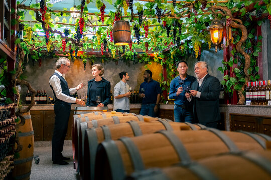 Group of Professional sommelier tasting and smelling red wine in wine glass at wine cellar with wooden barrel in wine factory. Winery liquor manufacturing industry and winemaker business concept.