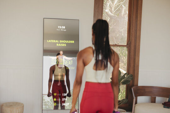 Young woman using a smart fitness mirror for virtual workout class