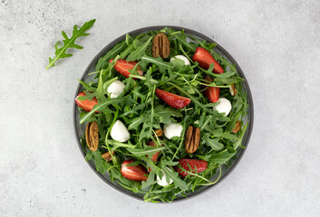 Salad with strawberries, mozzarella balls, arugula and pecans on gray background. Top view. 