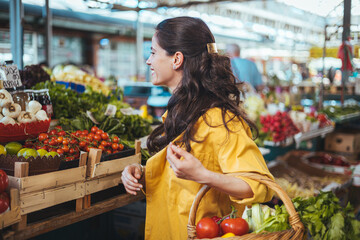 View at young woman buying vegetables at the market. A woman shops in a local outdoor agriculture market with fresh, organic local fruits and vegetables. 