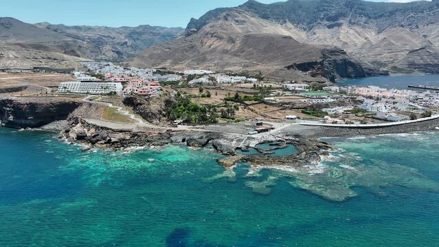 Fantastic aerial shot in orbit and at a medium distance from the coast and where the hotels and buildings on the coast of the port of Agaete are located on a sunny day and the island of Gran Canaria.