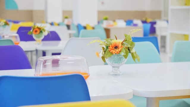 Small bouquet and empty transparent plastic bread holder on table in school canteen. Floral ornament for table in comfortable public cafeteria