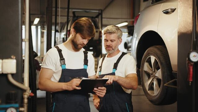 Mechanic man shows report on a tablet to the caucasian coworker at garage, A man mechanic and his son discussing repairs done vehicle. Changing automobile business. Auto Repair Estimate Car service