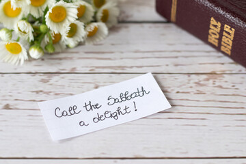 Christian Sabbath rest handwritten note with closed holy bible and flowers on wooden table. Delight...