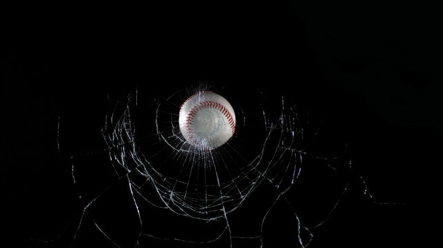 Ball of Baseball breaking Pane of Glass against Black Background