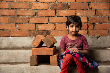 Indian asian Labour girl child posing besides conceptual brick house at construction site