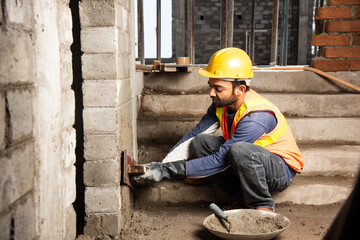 Happy Indian male construction worker constructing brick wall - hard working concept, manual labour