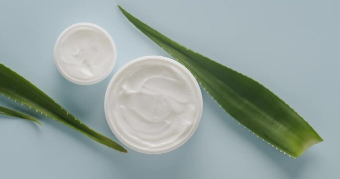 White Bottles and tubes with aloe vera plant rotating for cosmetics on a light blue background in studio. Cosmetics oils based on natural ingredients, scrub, tonic, body care. Top view.