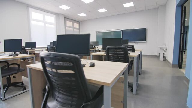 Computers on small wooden desks in empty IT classroom closeup. Digital equipment for students and teacher workplace in college