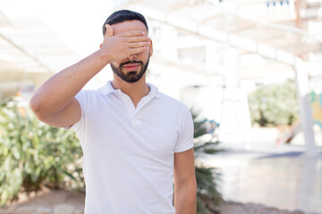 Fototapeta premium young handsome man covering eyes with one hand feeling scared or anxious, wondering or blindly waiting for a surprise