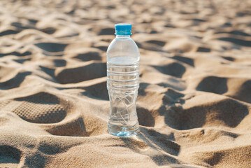 Bottle of water standing on sand, refreshing cold drink in desert on hot sunny day